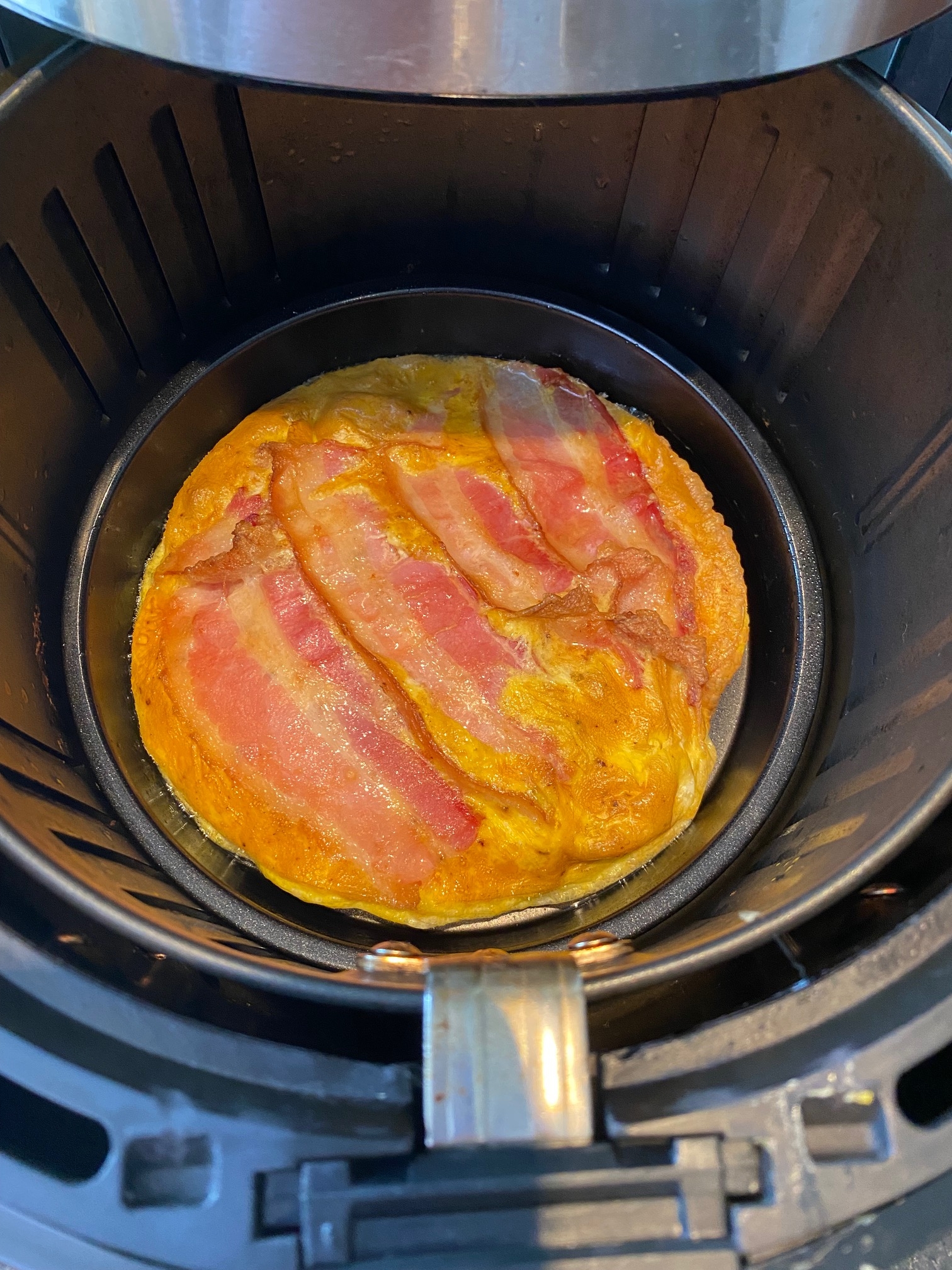 Cooked bacon and eggs in the air fryer basket.