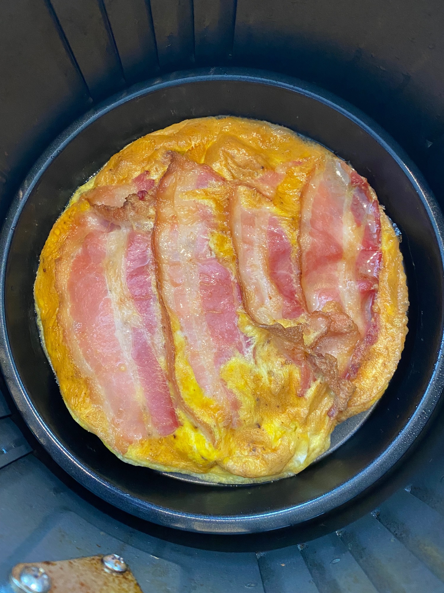 Cooked bacon and eggs in the air fryer basket.