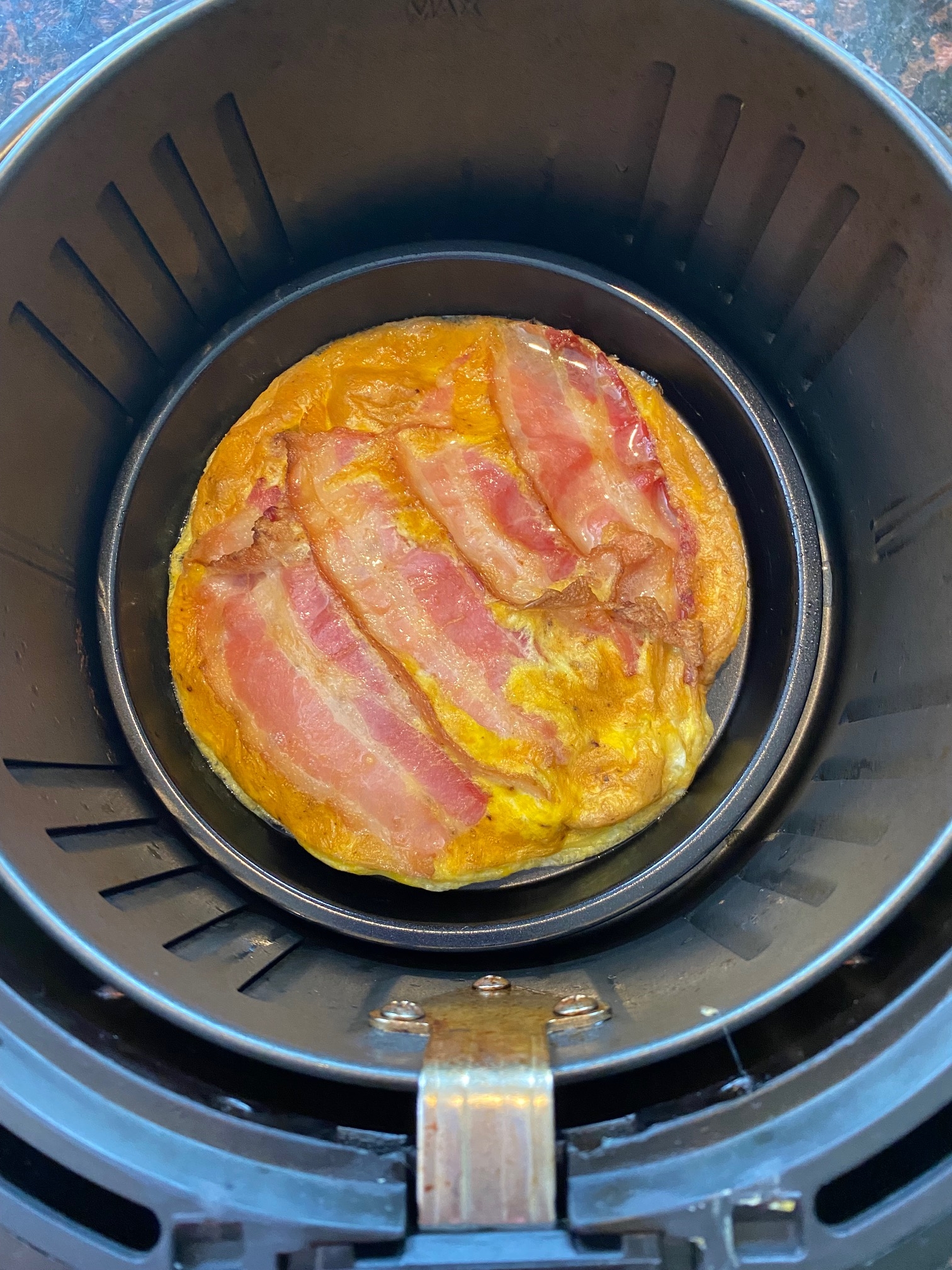 Cooked bacon and eggs in the air fryer basket.