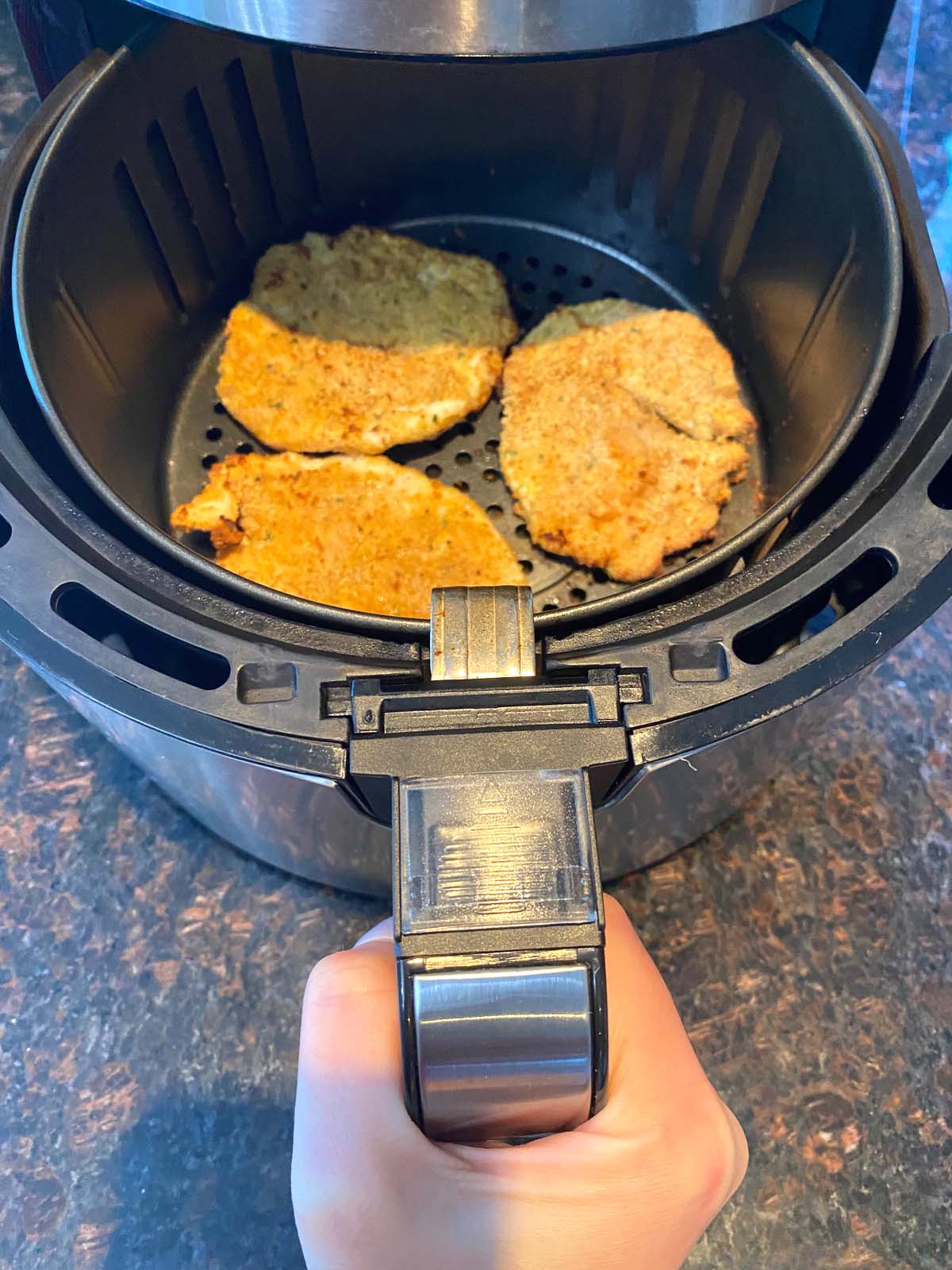 Hand partially removing basket to show crispy turkey slices.