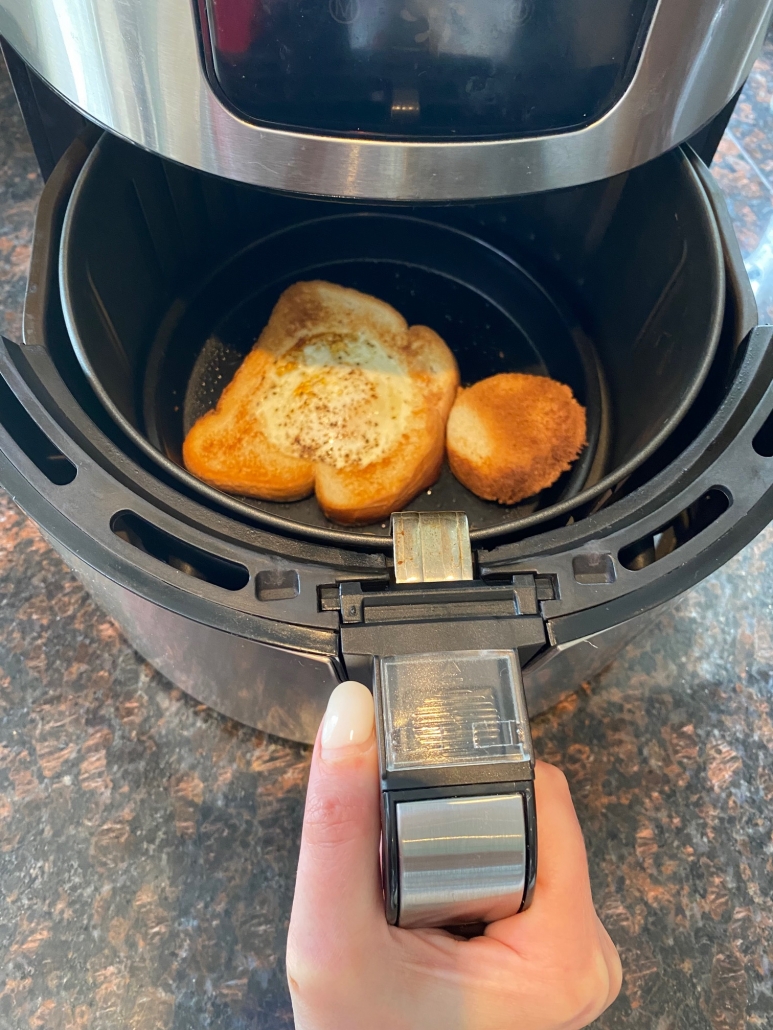 Hand holding air fryer basket with egg in a hole toast inside
