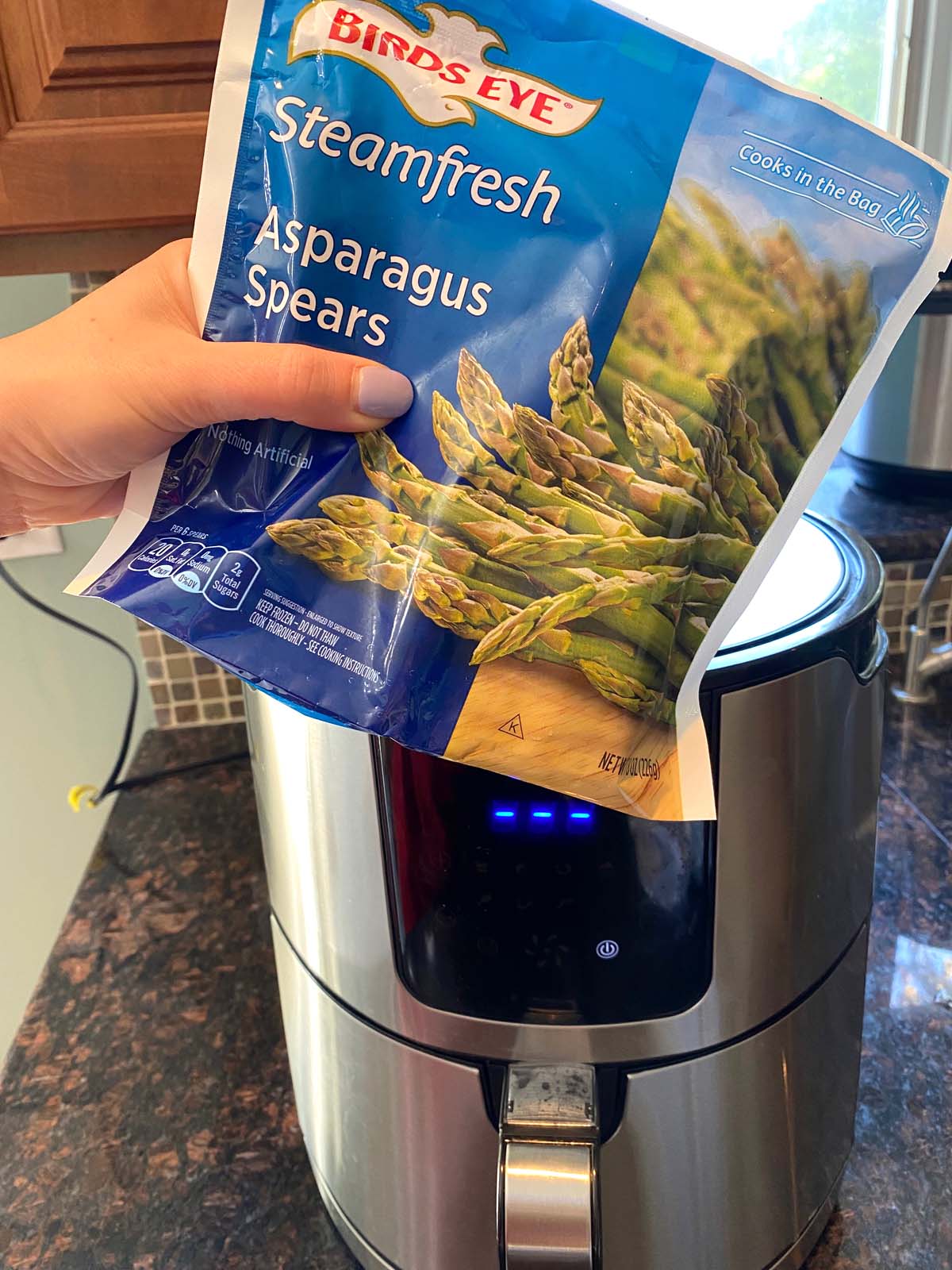 A bag of frozen asparagus in front of an air fryer.