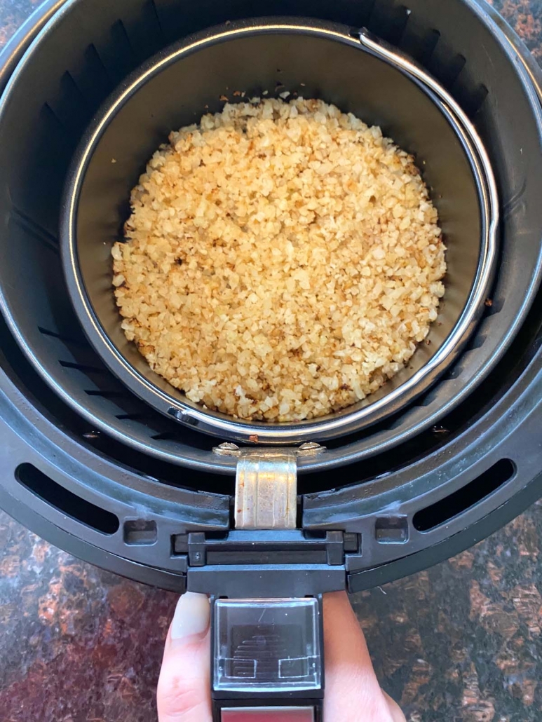 hand holding air fryer with cauliflower rice inside