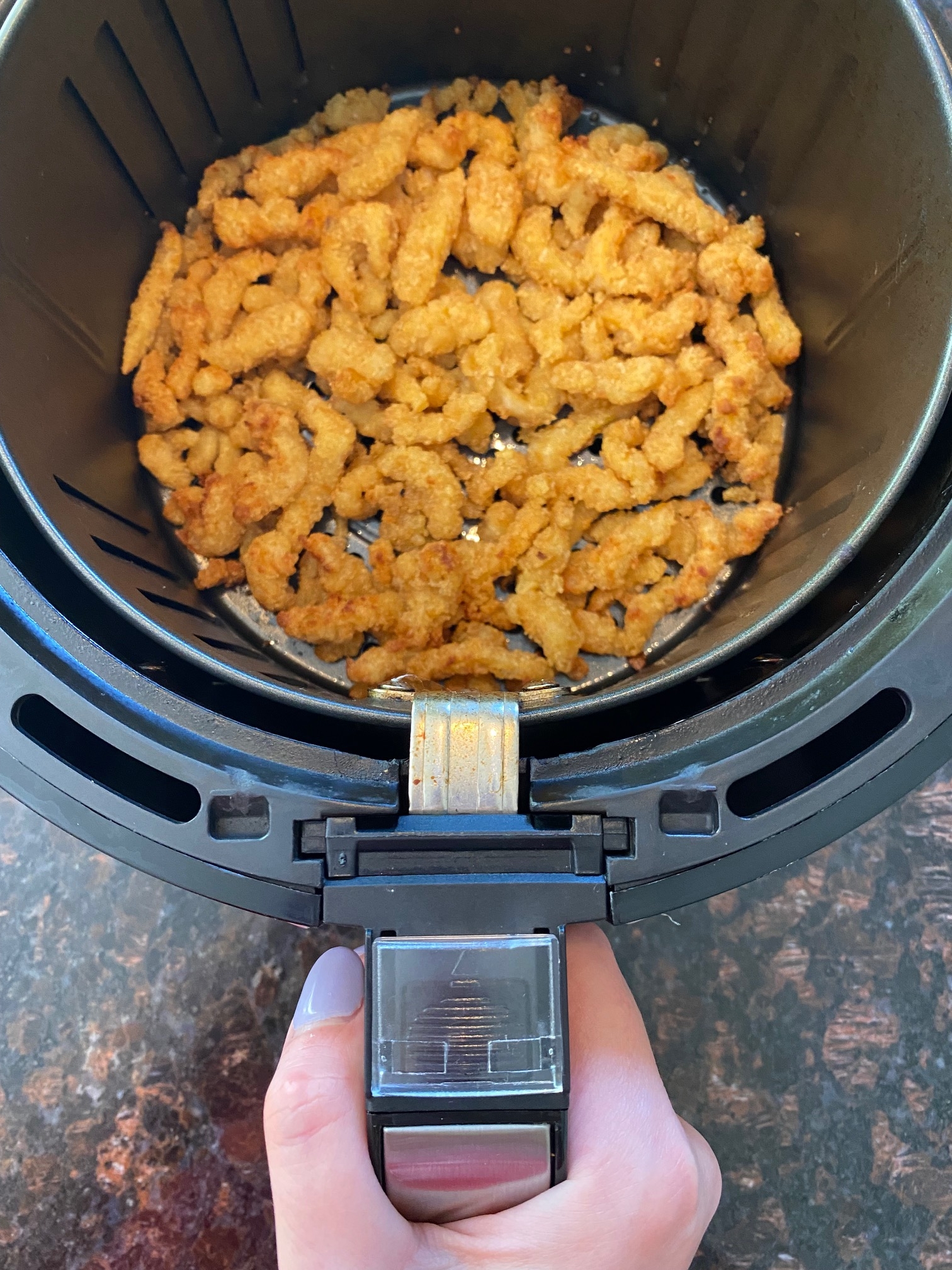 Hand removing basket from tabletop convection oven with cooked clam strips in it.
