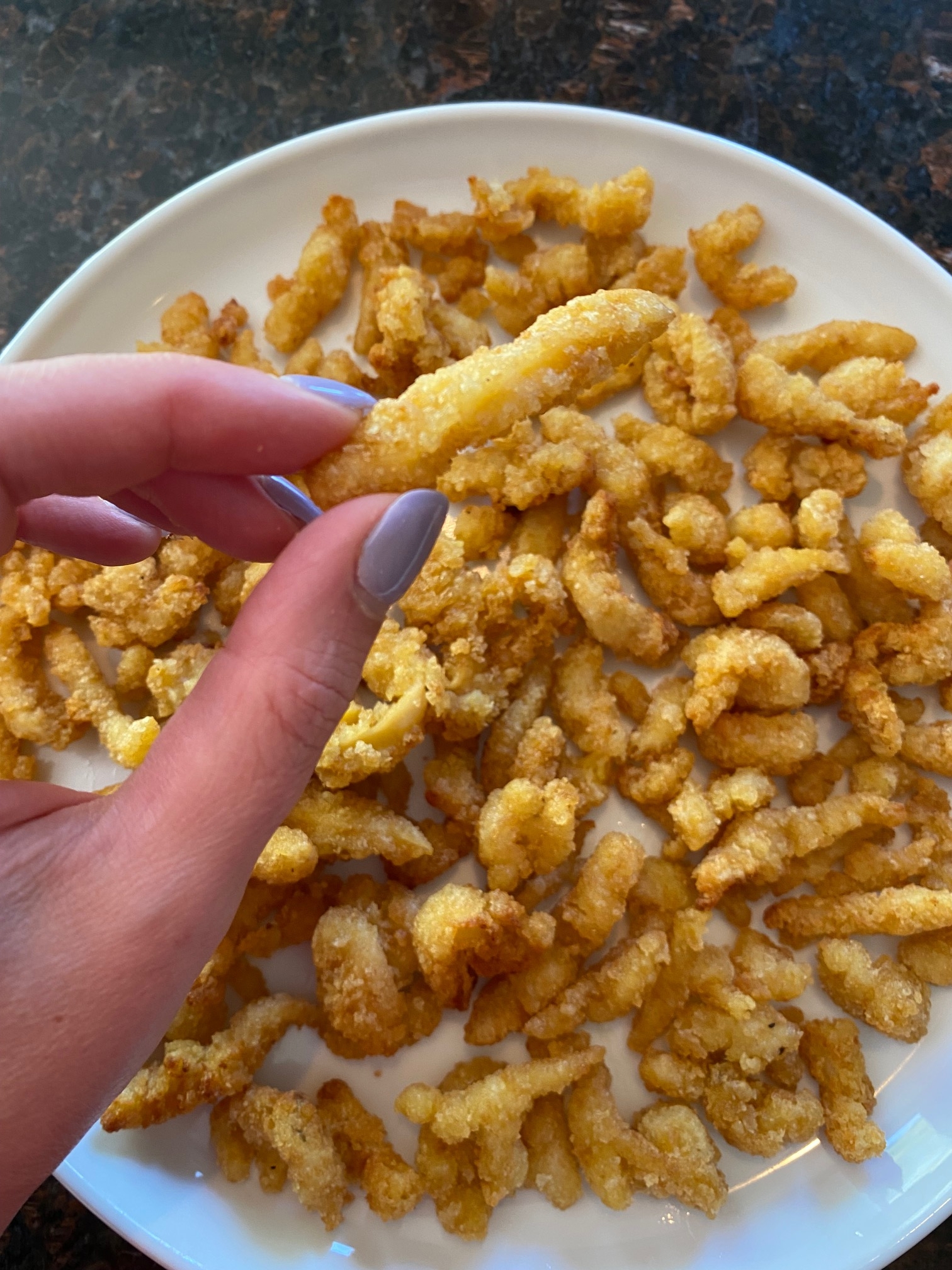 Hand holding a clam strip with more below..