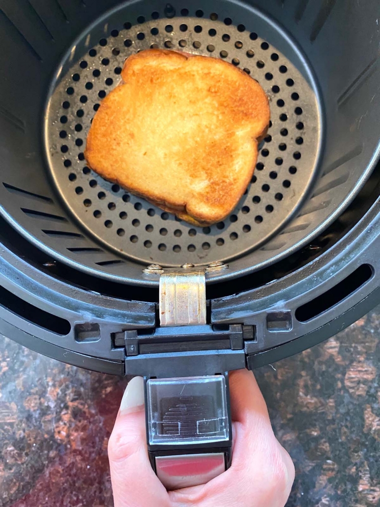 hand holding air fryer basket with toasted sandwich inside