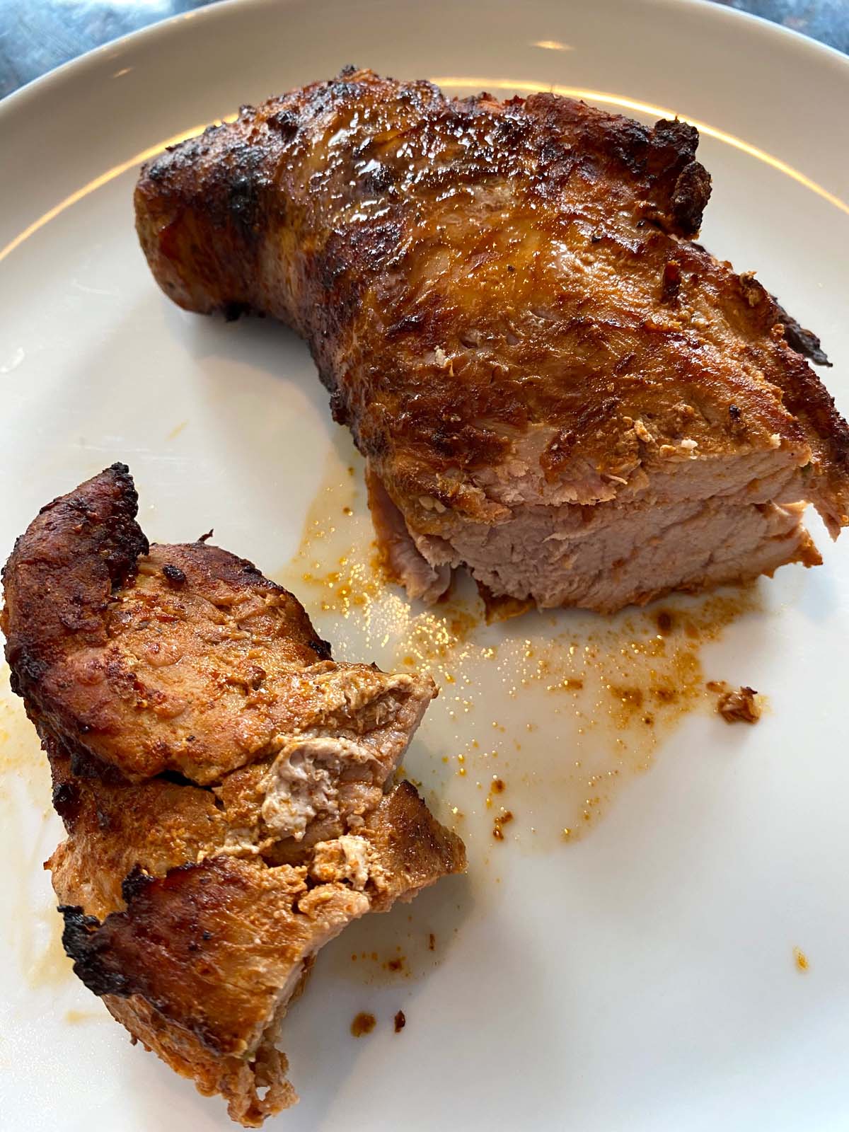 Cooked pork tenderloin cut in half on a white plate.
