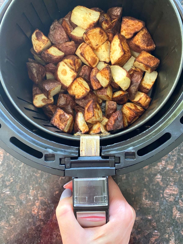 hand holding air fryer basket with potatoes inside