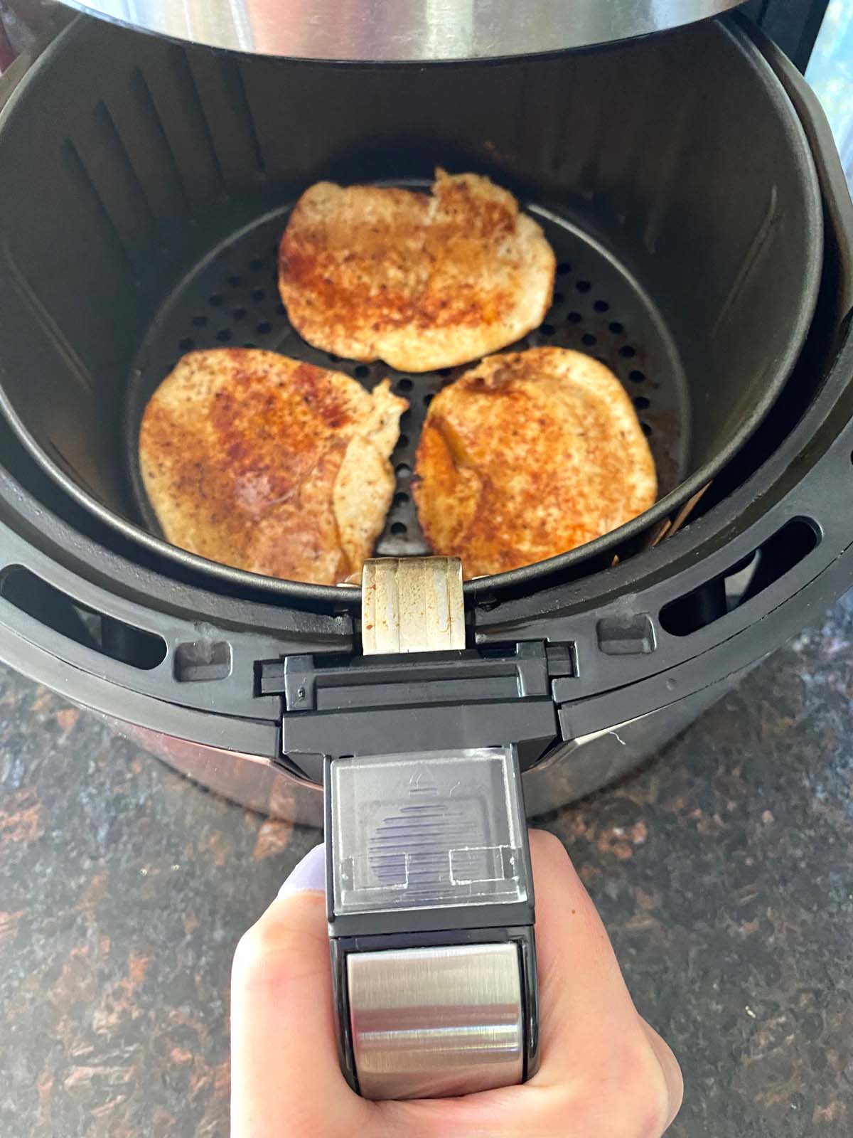 Pulling air fryer basket out with 3 cooked turkey cutlets in basket.