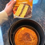 Baked yellow cake in an air fryer with a box of yellow cake mix being held next to it.