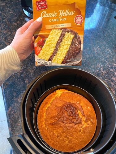 Baked yellow cake in an air fryer with a box of yellow cake mix being held next to it.