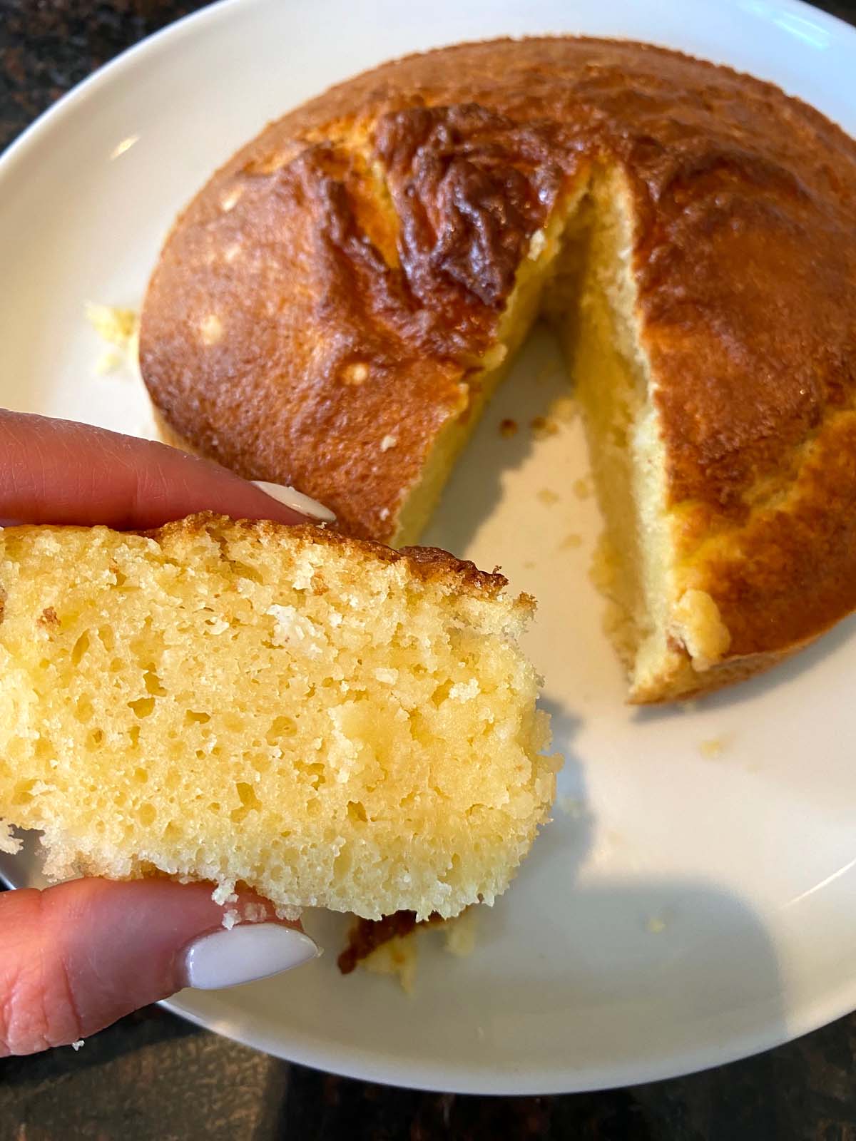 Yellow cake on a plate with slice cut out and slice held up.