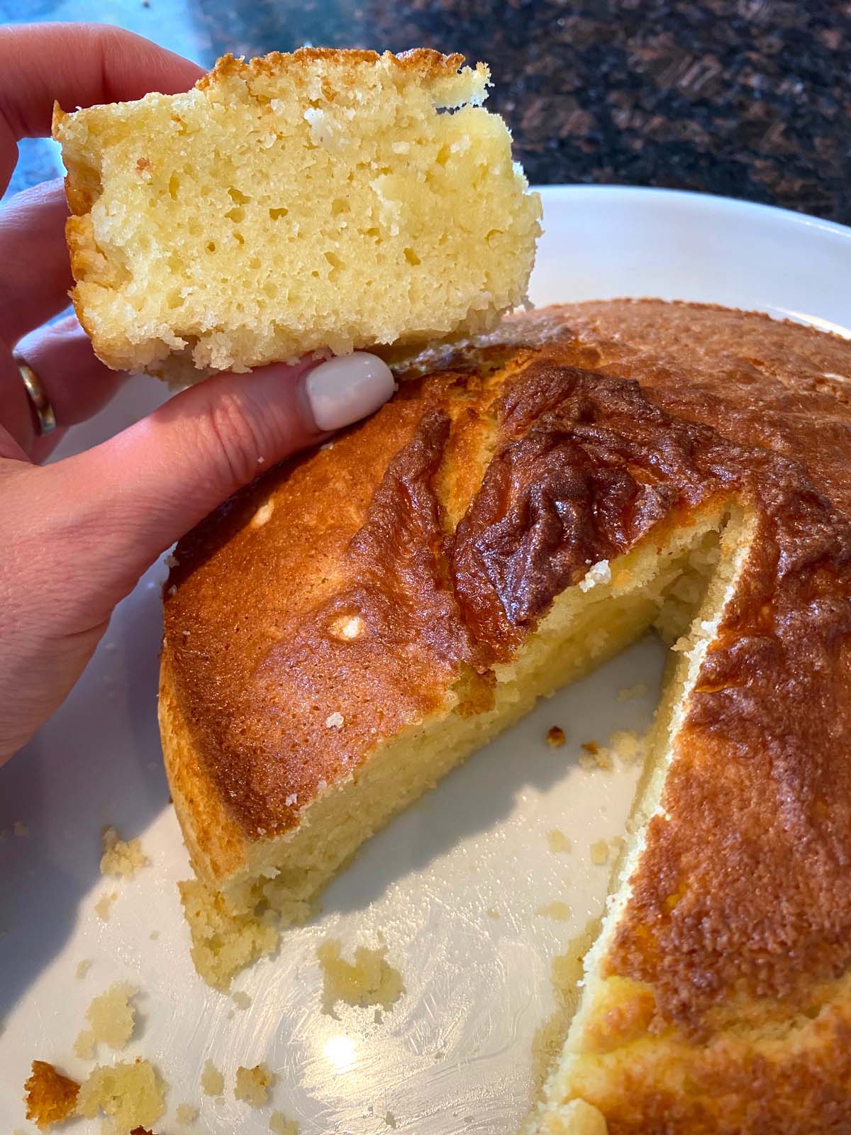 Yellow cake on a plate with slice cut out and slice held up.