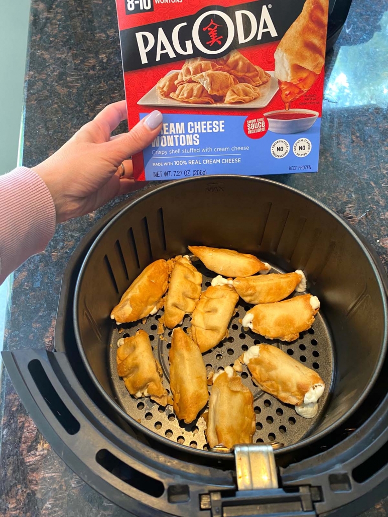 hand holding package of frozen cream cheese wontons above air fryer basket with wontons inside