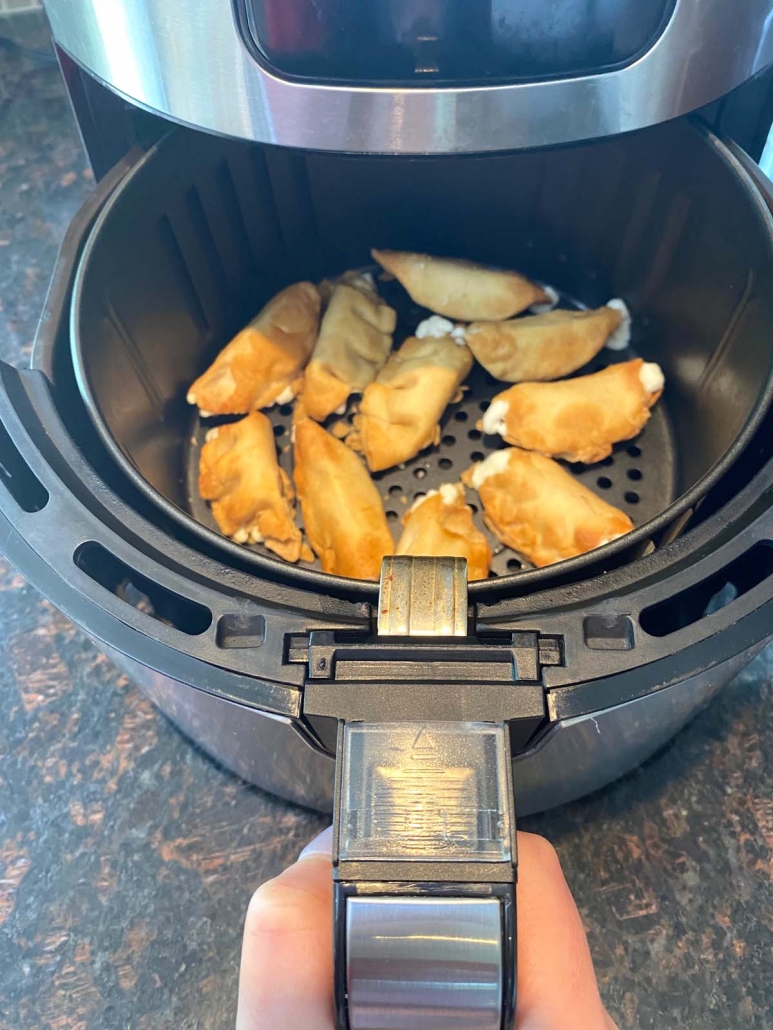 hand holding air fryer basket filled with frozen cream cheese wontons