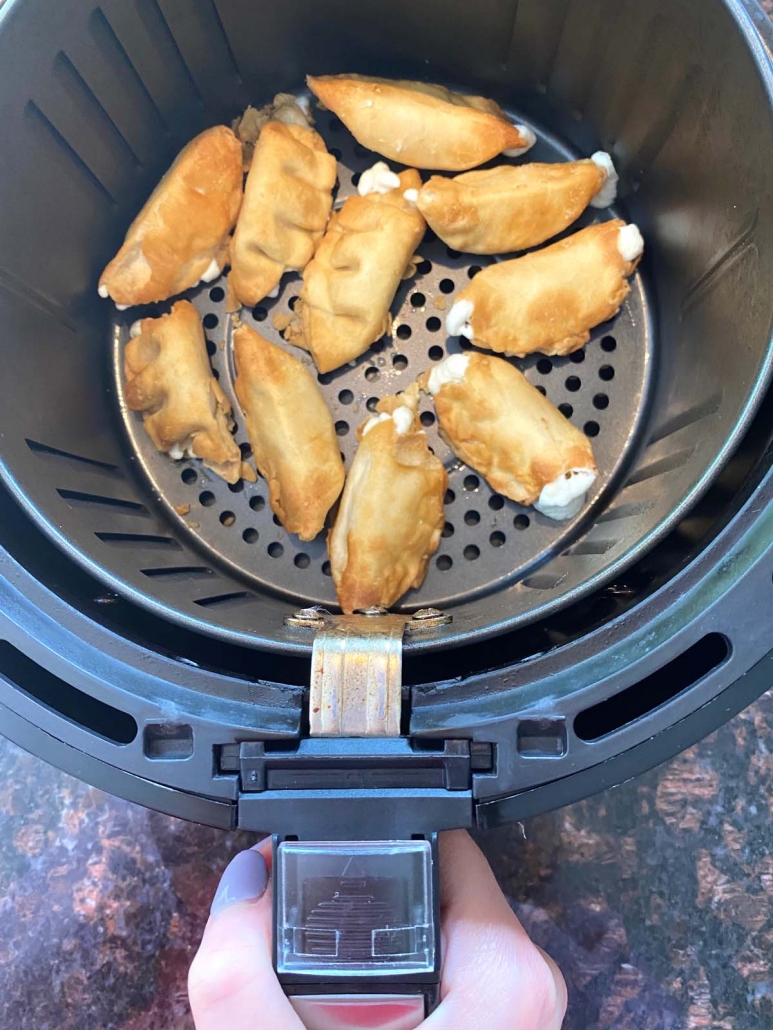 hand holding air fryer basket filled with air fried cream cheese wontons