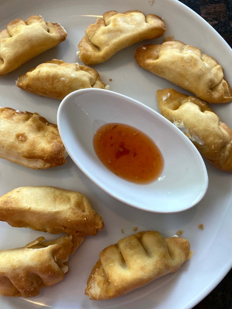 air fried cream cheese wontons on a plate with small bowl of dipping sauce in the middle