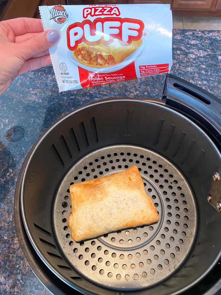 hand holding package of pizza puff above air fryer basket with pizza puff inside