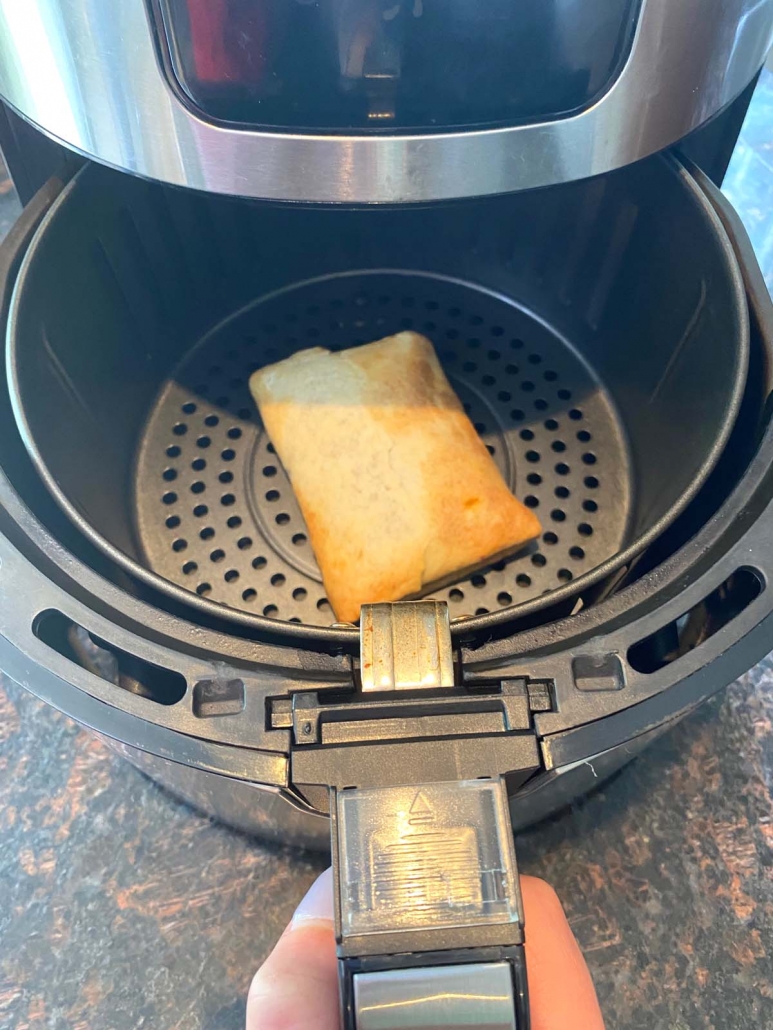 hand holding air fryer basket with frozen pizza puff inside