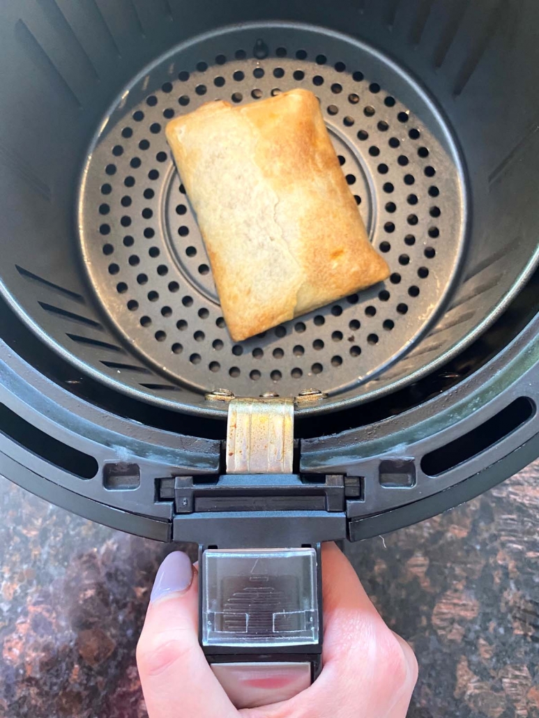 hand holding air fryer basket with pizza puff inside