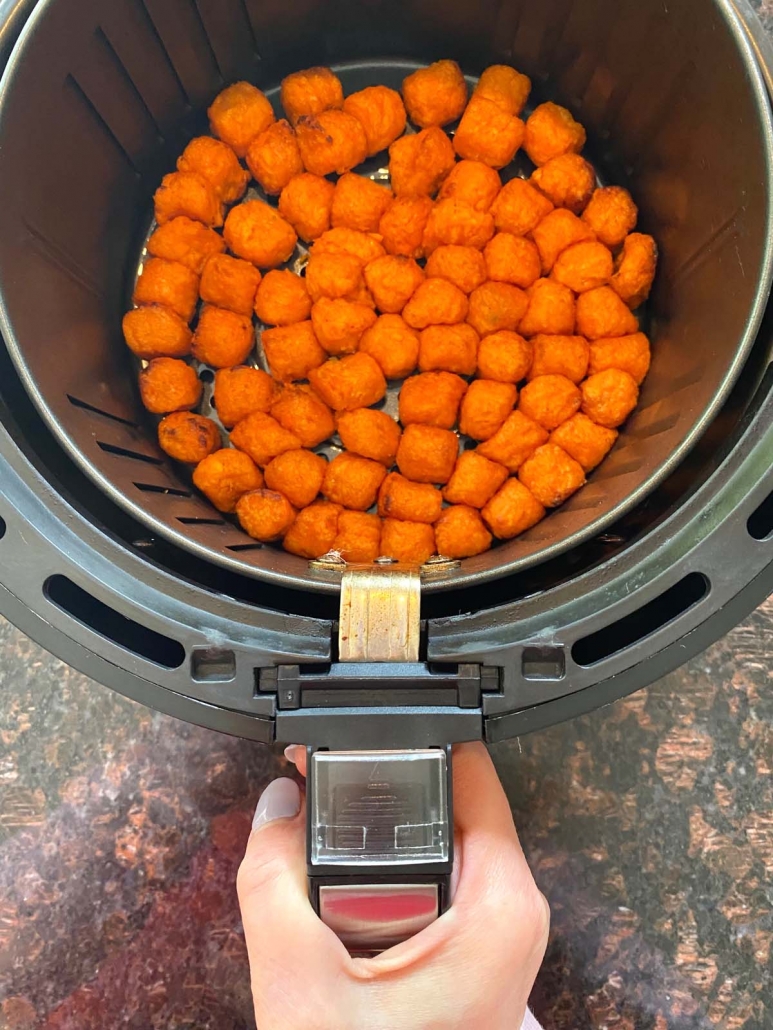hand holding the air fryer basket with sweet potato puffs inside