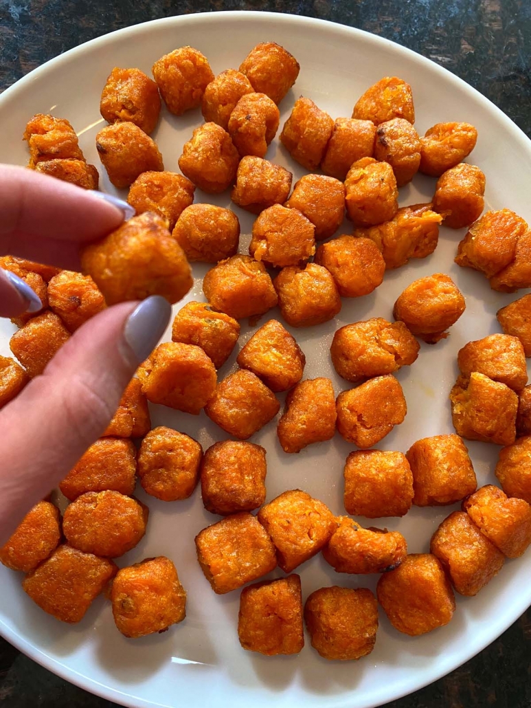 hand holding a single air fried sweet potato puff above a plate filled with more