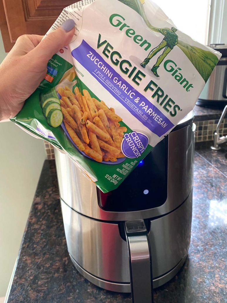 hand holding bag of frozen zucchini fries in front of the air fryer