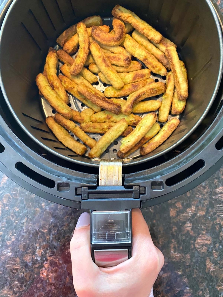 hand holding air fryer basket with zucchini fries inside