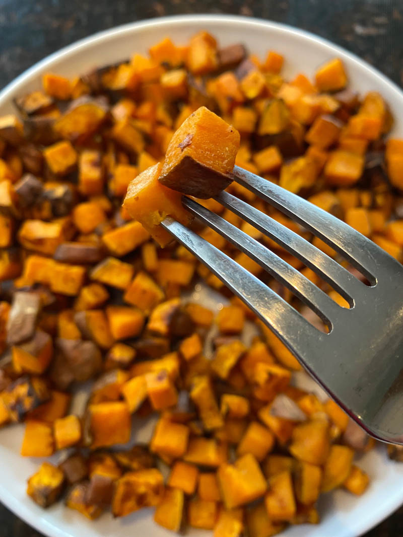 Plate of cooked diced sweet potatoes with a fork hold one up.