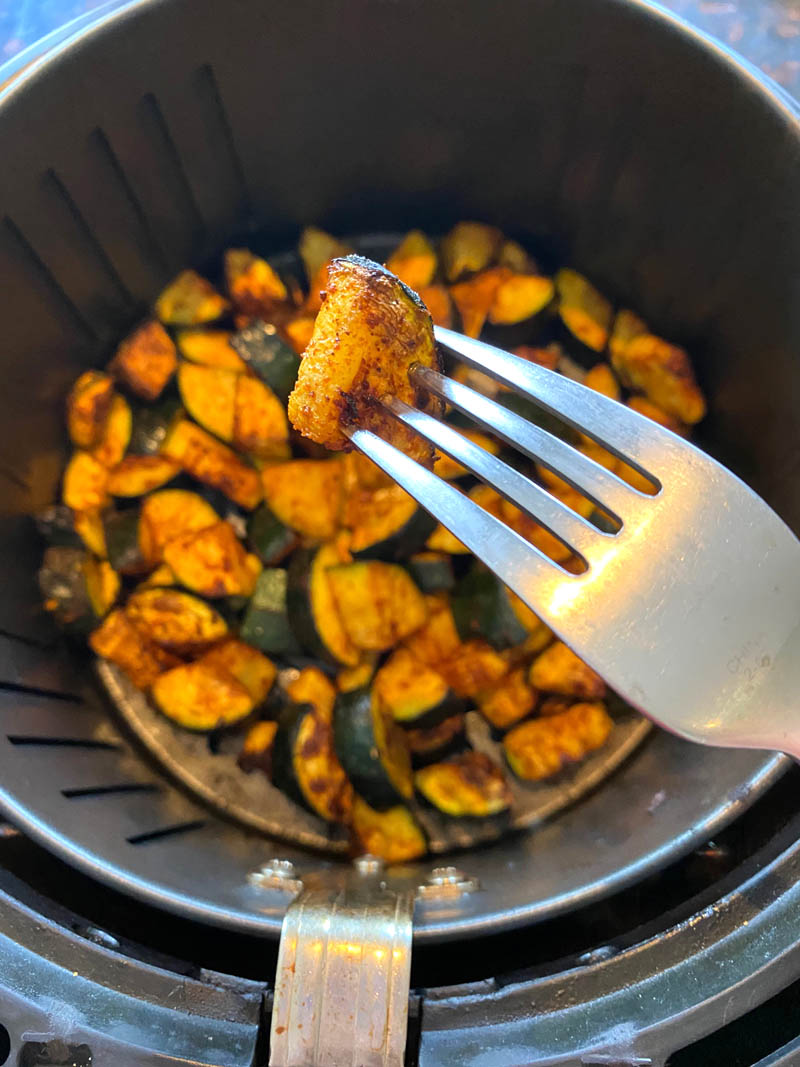 Spicy zucchini in an air fryer with a fork holding on bite.