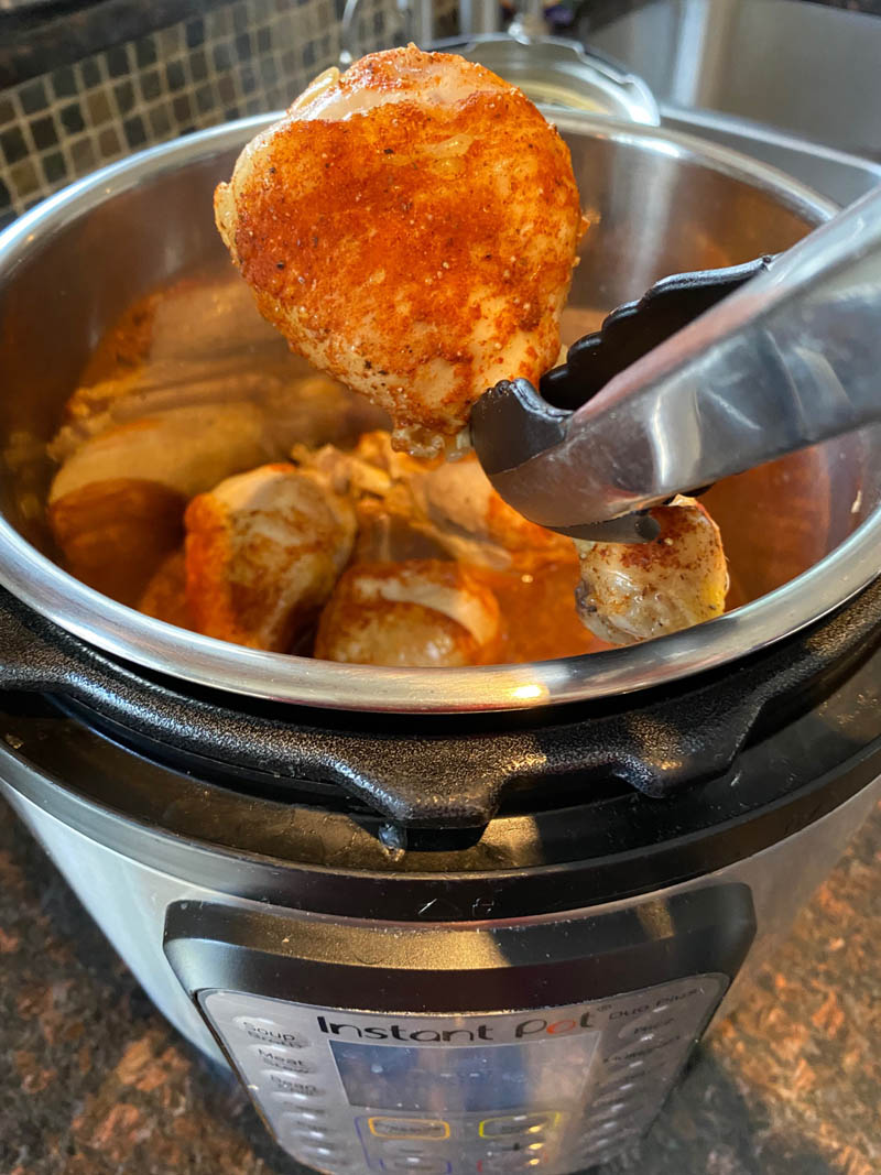 Tongs pulling out 1 chicken drumstick from instant pot to show texture.