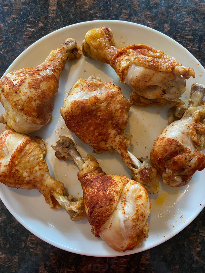 White plate with 6 seasoned chicken drumsticks.