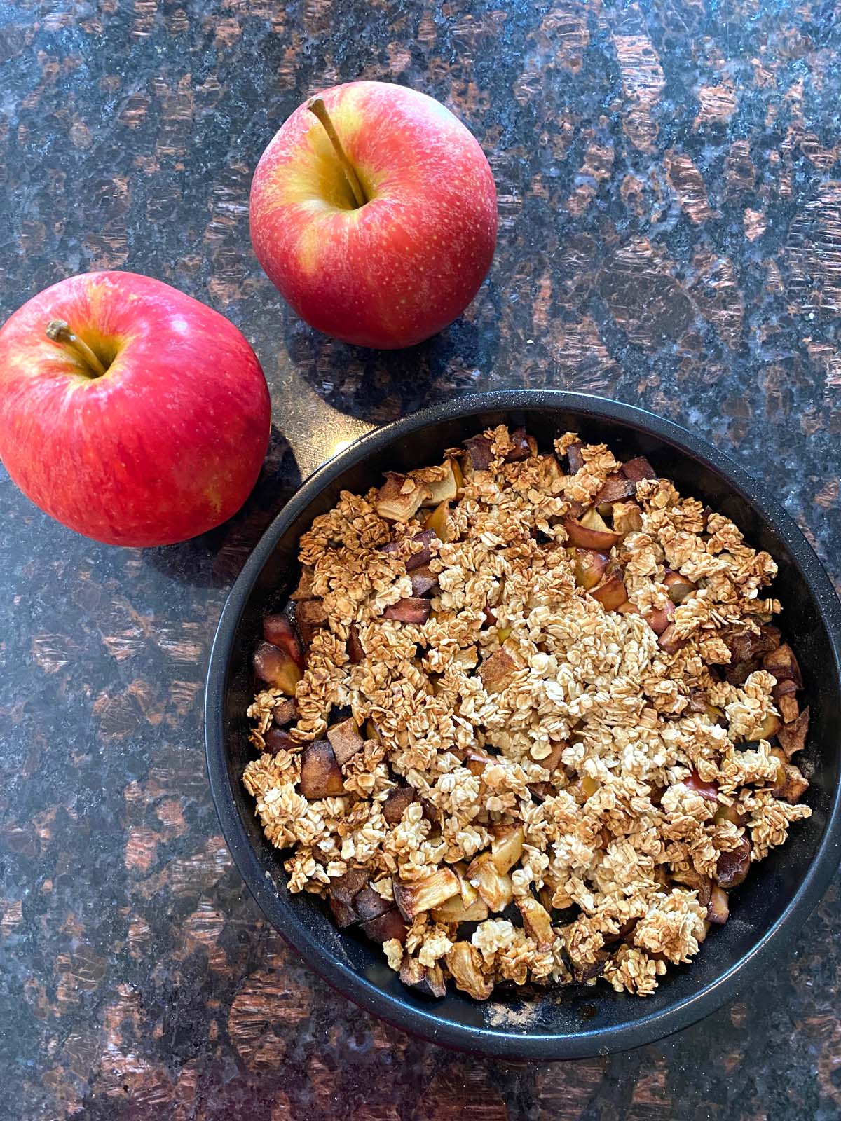 Apple crumbled in a pan with 2 apples next to it.