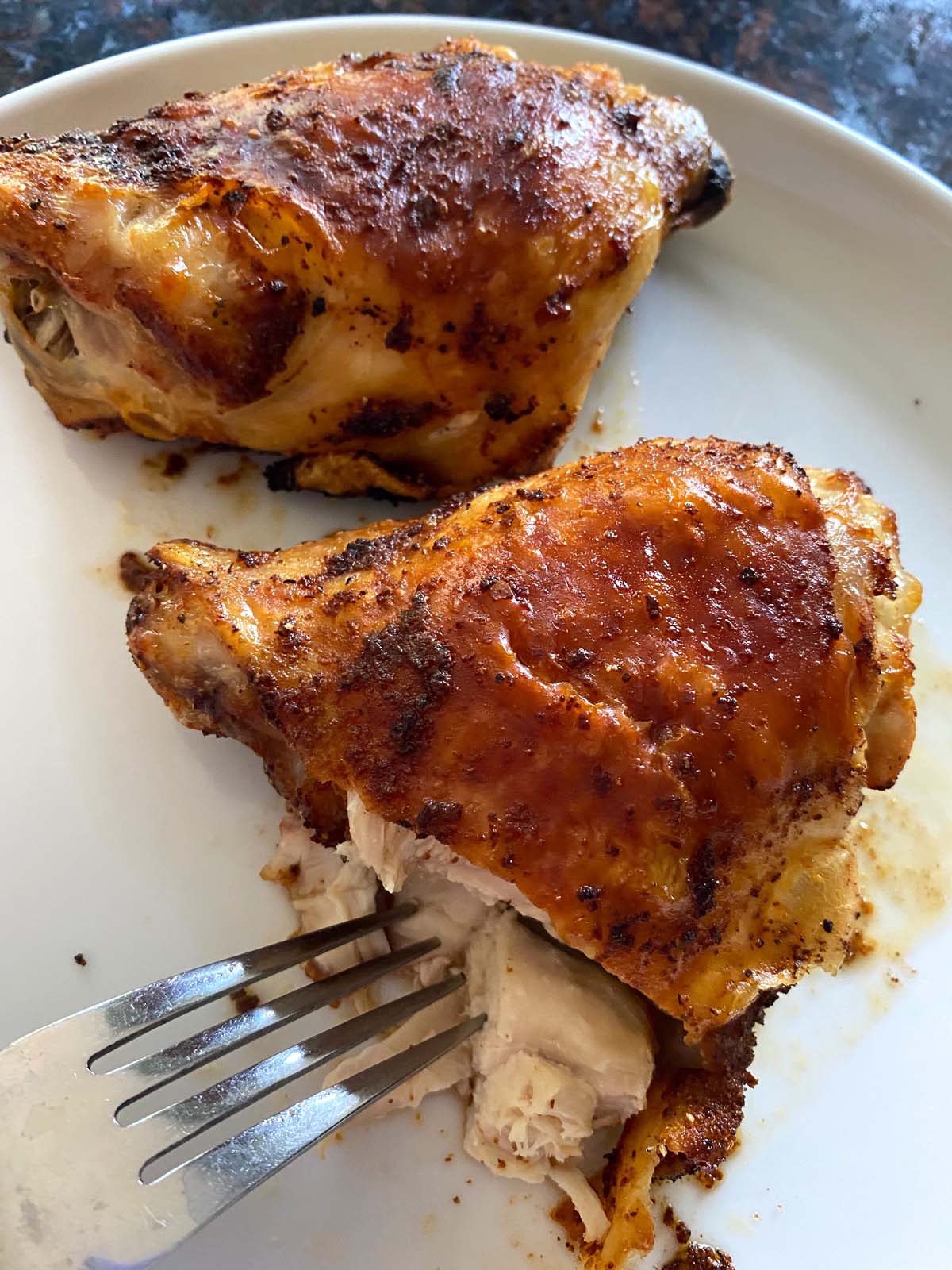 Cooked chicken thighs on a white plate.