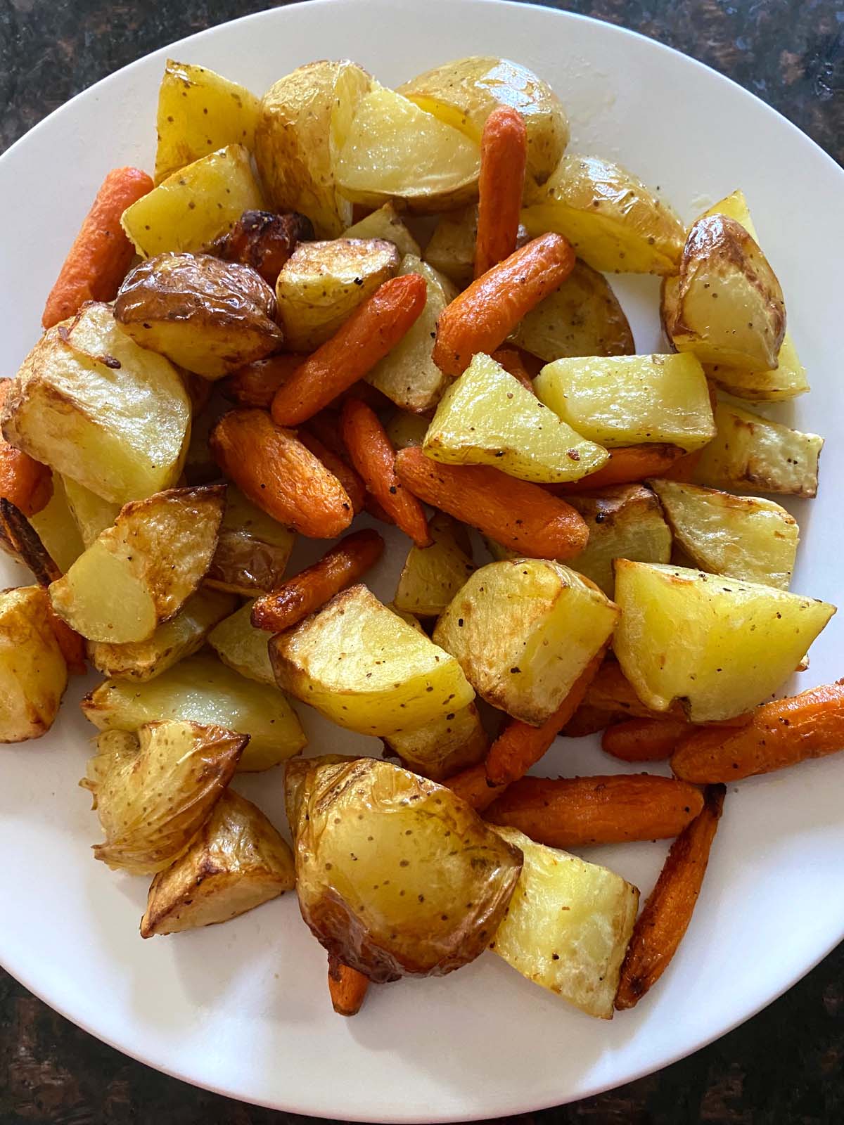 Roasted potatoes and carrots on a white plate.