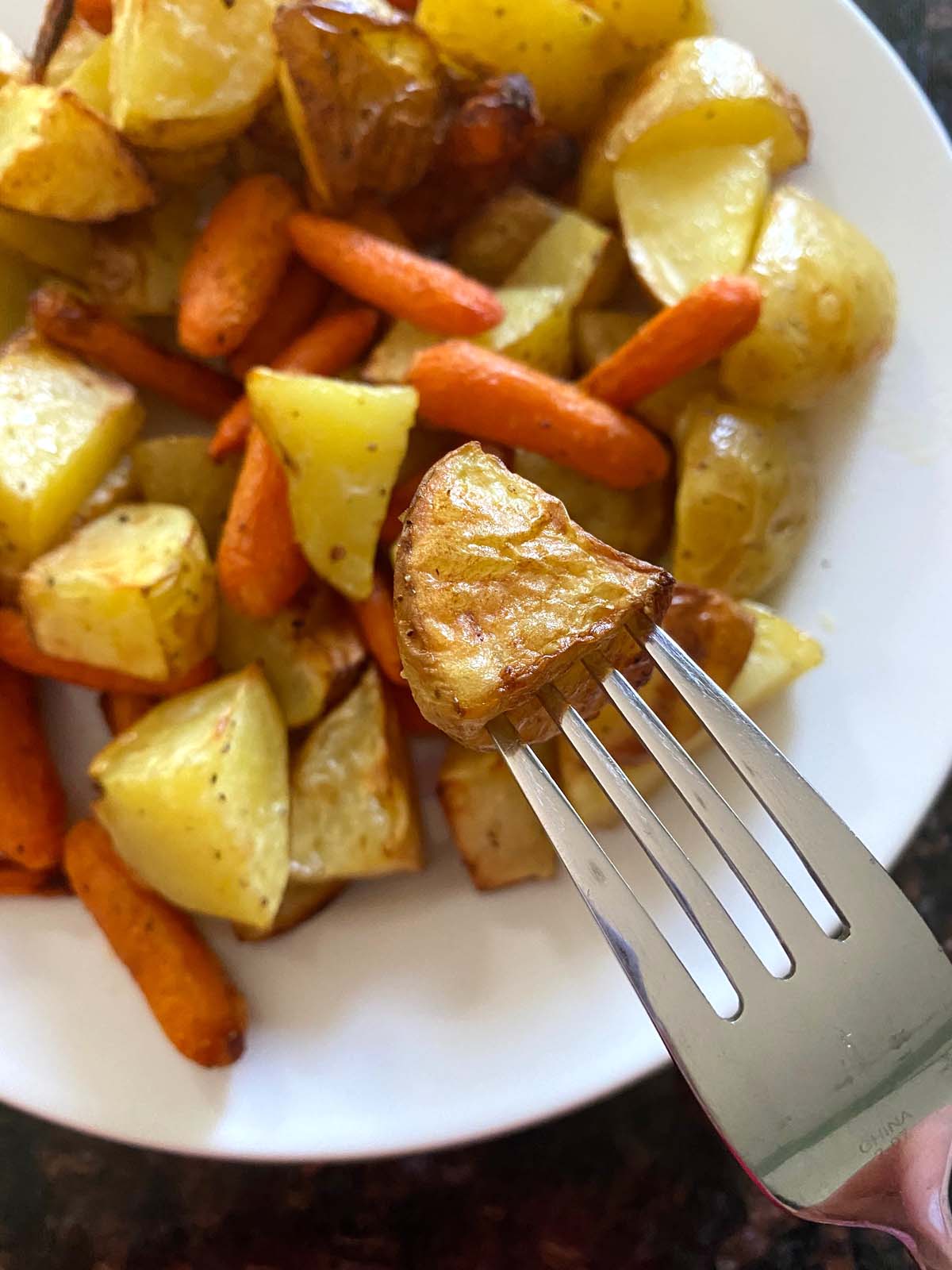 Roasted potatoes and carrots on a white plate.