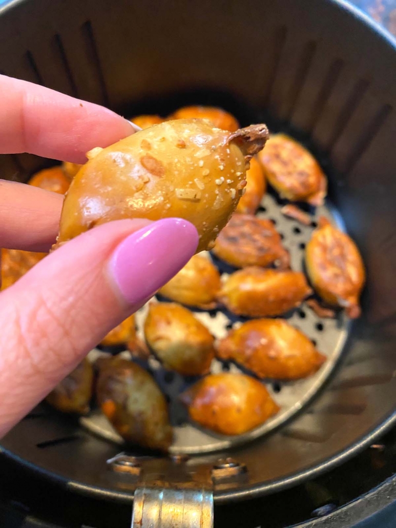 hand holding cooked pretzel bite in front of air fryer basket