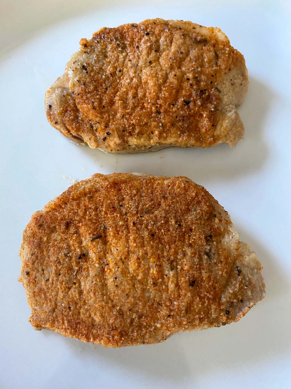 Thick cut boneless pork chops on plate with seasonings.