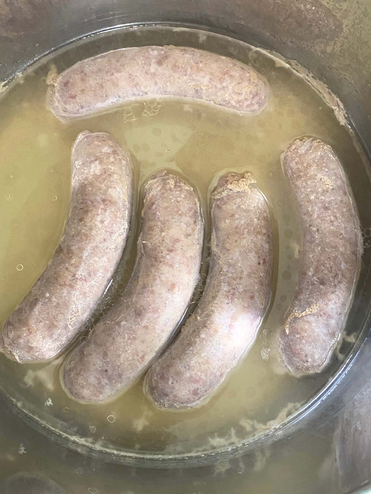 5 cooked brats in liquid after cooking.