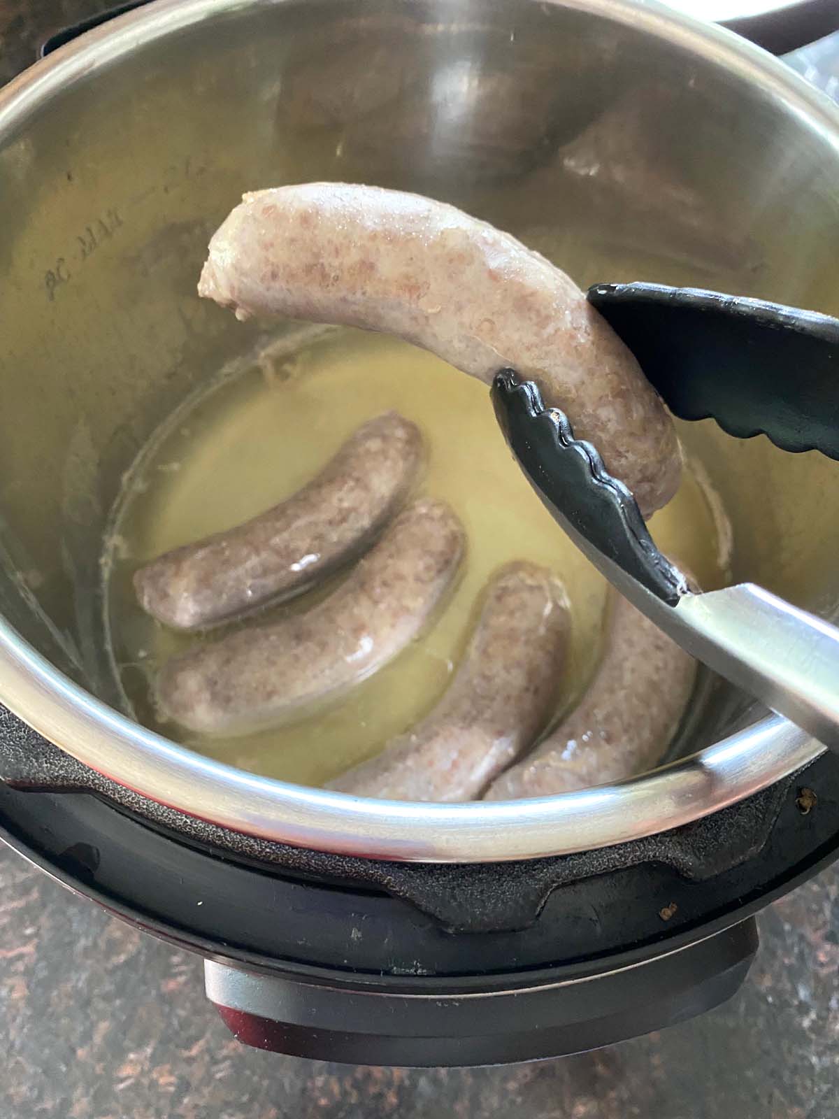 Tongs holding a cooked sausage over pot.