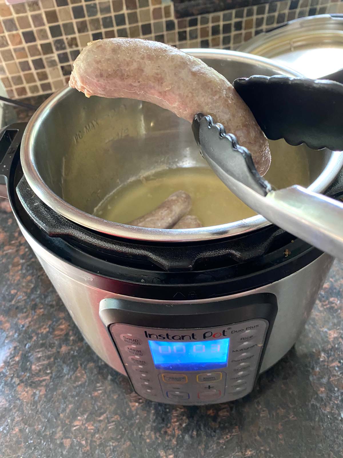 Tongs removing a cooked brat from pressure cooker.