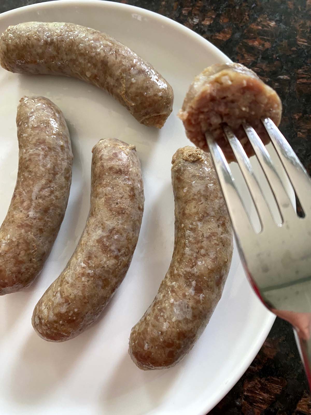 Plate of sausages after cooking with a piece on a fork.