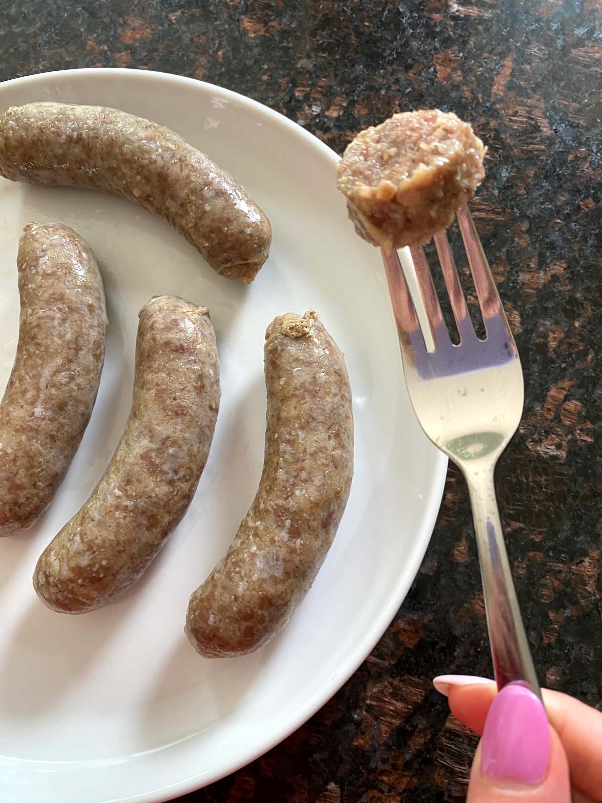Fork holding a slice of sausage over a plate of brats.