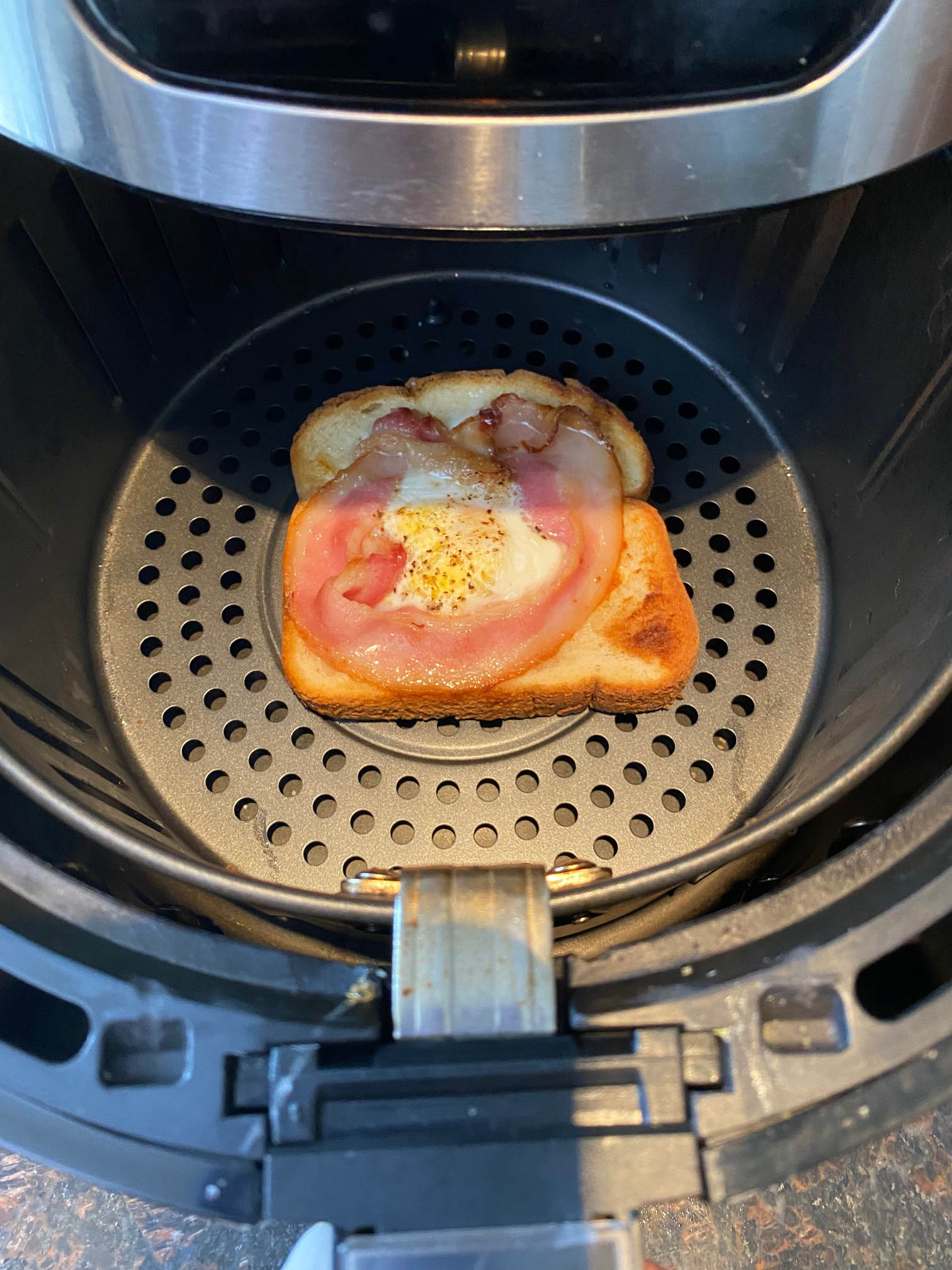 Toast with soft bacon and over easy egg in the basket of tabletop convection oven.