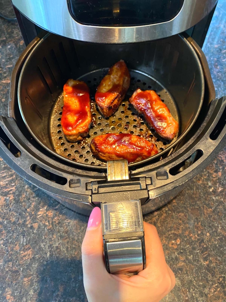 hand pulling out air fryer basket with pork ribs inside