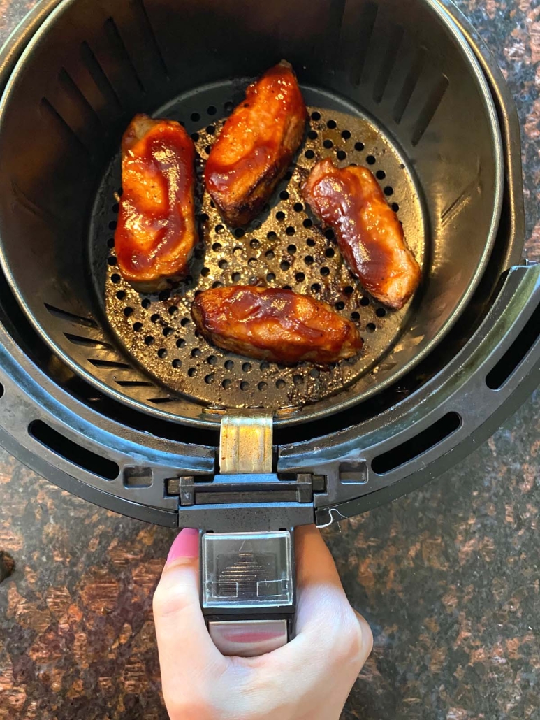 hand holding air fryer with pork ribs inside