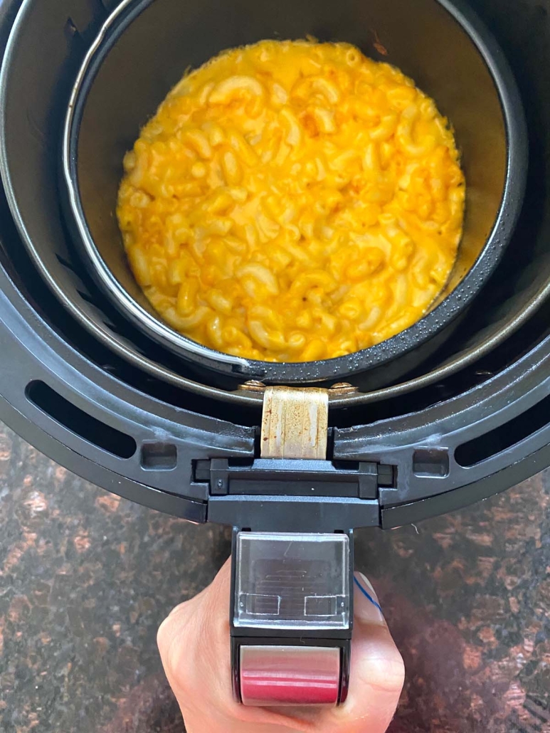 hand holding air fryer basket with pan filled with mac and cheese
