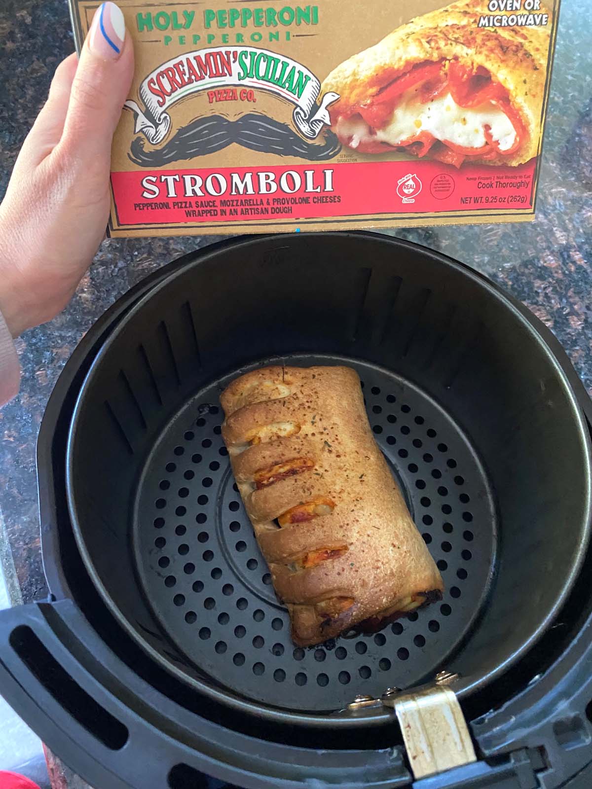 Cooked stromboli in the air fryer with a package of stromboli being shown.