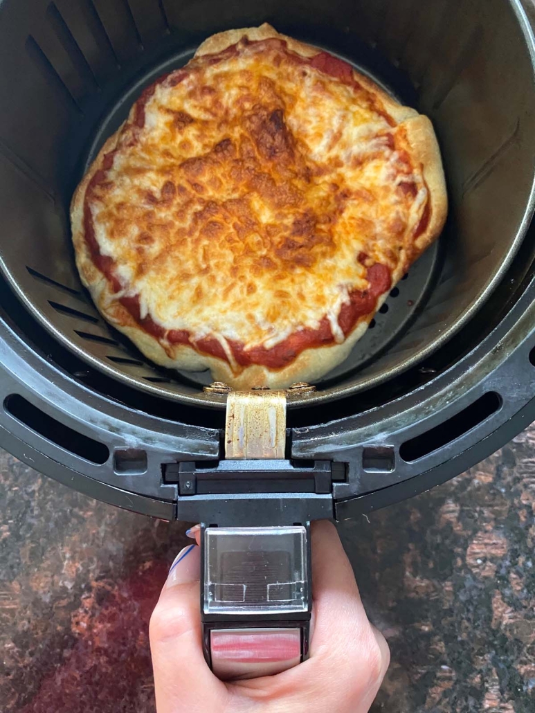 hand holding air fryer basket with pizza inside