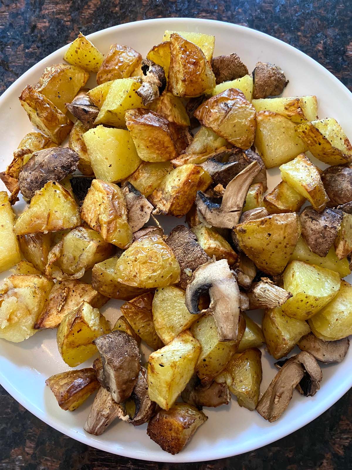 Cooked potatoes and mushrooms on a white plate.